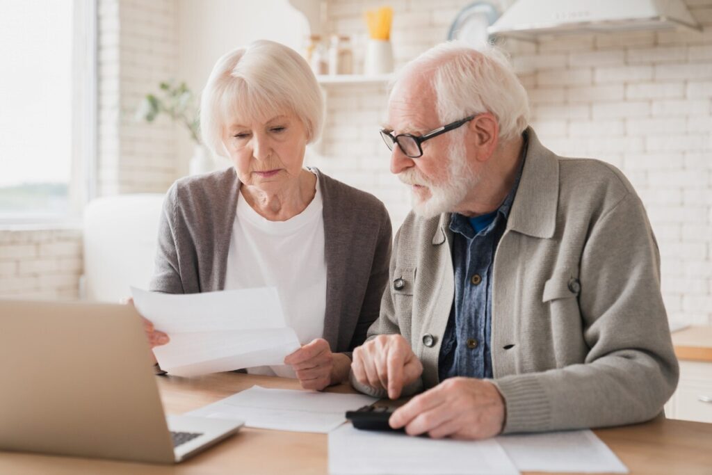 A senior couple looks at papers and a laptop as they conduct research