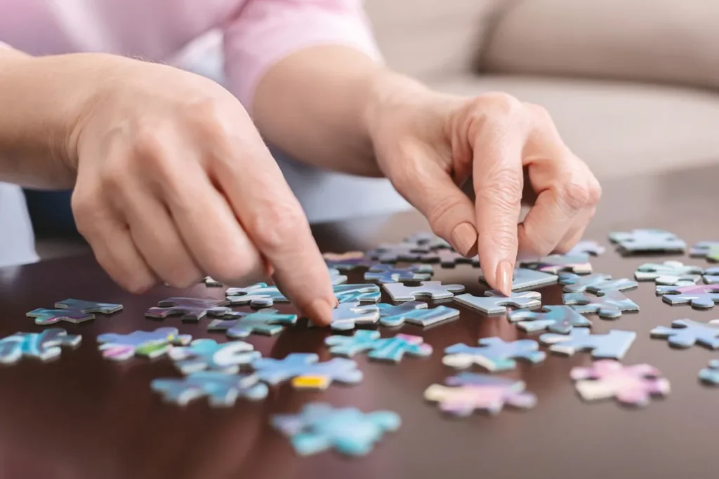 A senior woman plays with a jigsaw puzzle on a flat surface.