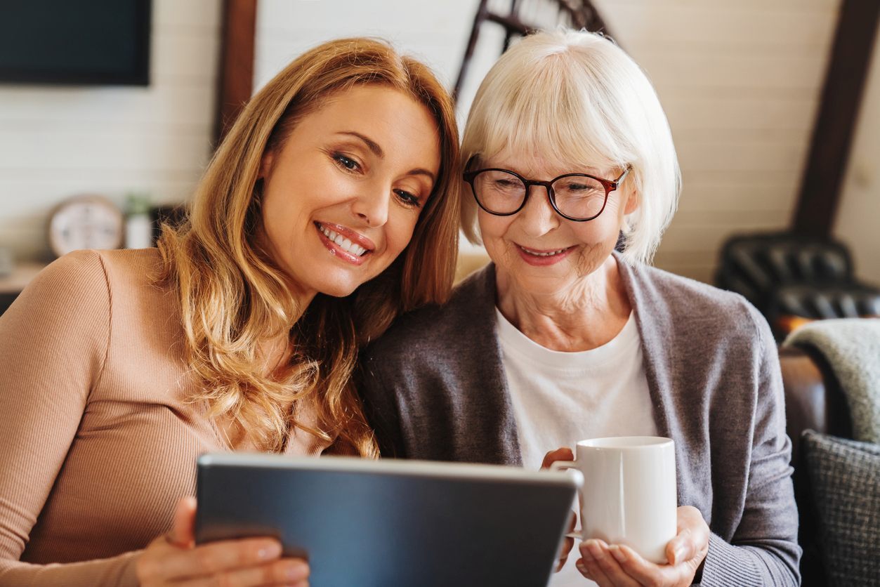 A smiling senior woman and her adult daughter use a tablet together.