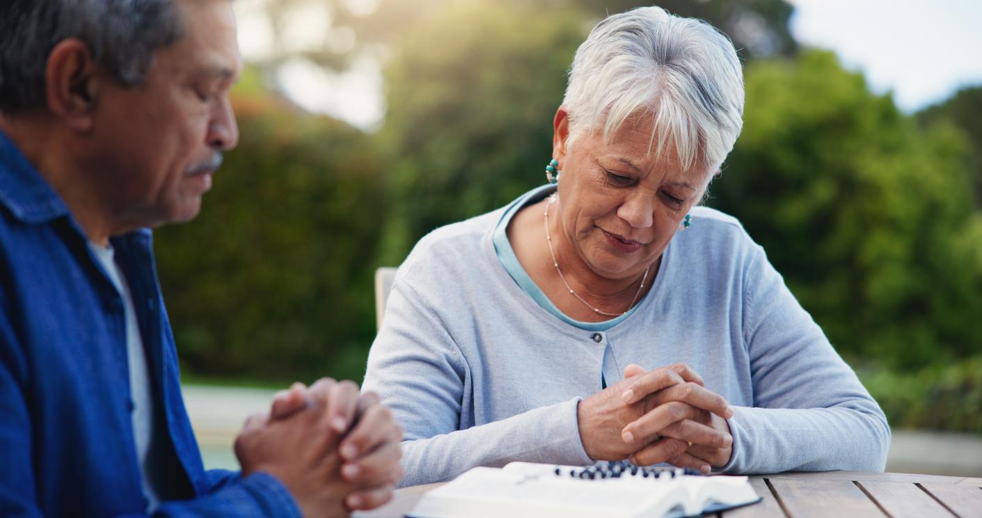 An elderly couple prays at a faith-based event held in an outdoor space.