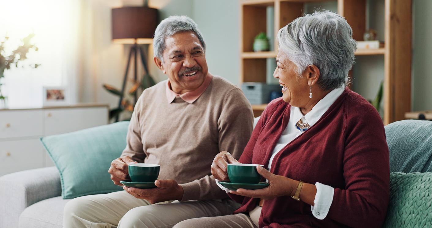 An elderly couple enjoys a cup of coffee and each other’s company on a living room sofa.