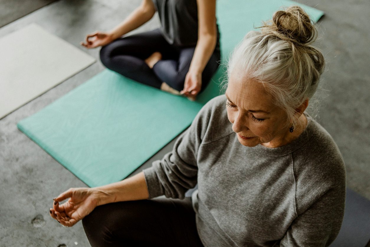 A senior woman meditates in a group session to achieve spiritual wellness.