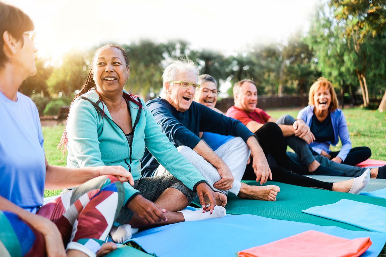 A group of happy seniors sitting on yoga mats outdoors.