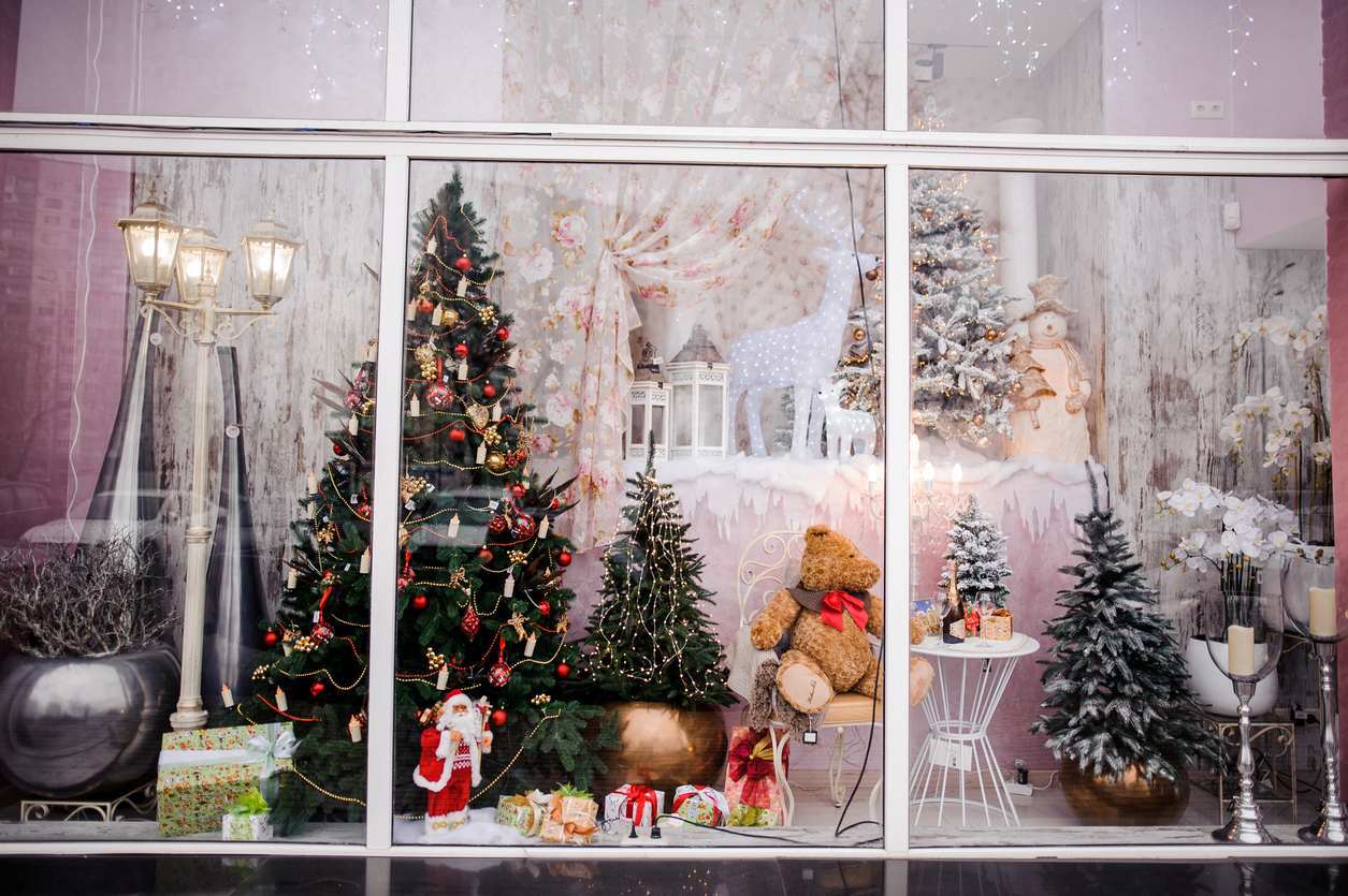 A beautiful festive Christmas windowfront filled with artificial trees, a Santa figurine, miniature lampposts, and toys.