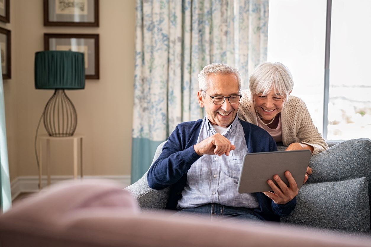 Senior couple smiling while using a digital tablet for a video call in an Americare assisted living community.