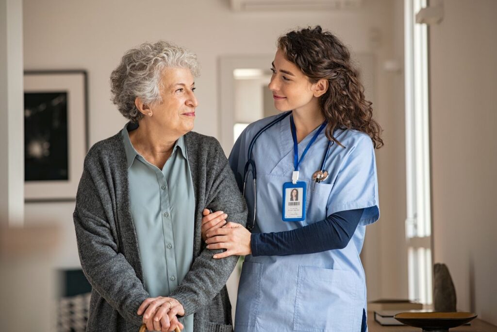 A nurse assists an elderly woman with a walking stick at a nursing home.